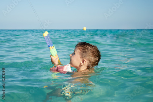 Foto Boy with floater  sleeves swimming in a sea and having fun with water pistol