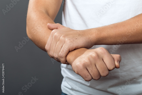 Close up, man hand holding his wrist on gray background