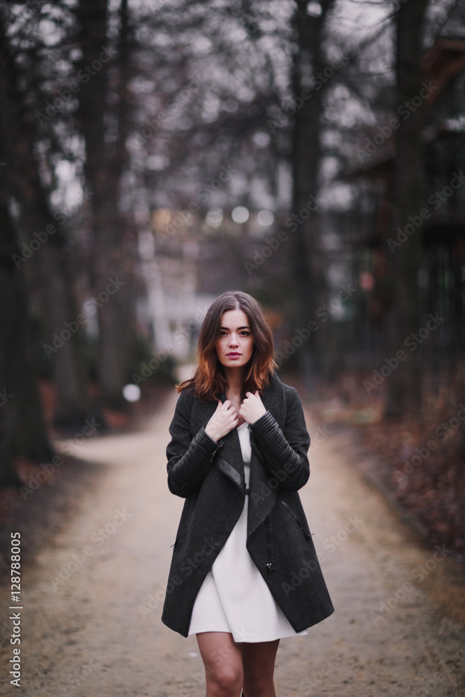 Attractive, charming young woman in a white cotton dress and dark coat walking in the autumn Park. Cloudy. Soft colors of nature. The melancholy mood. Attractive, charming young woman in a white cotton dress and dark coat walking in the autumn Park. Cloudy. Soft colors of nature. The melancholy mood.