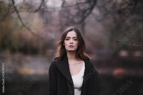 Obraz na płótnie Attractive, charming young woman in a white cotton dress and dark coat walking in the autumn Park