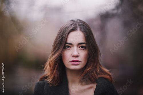 Attractive, charming young woman in a white cotton dress and dark coat walking in the autumn Park. Cloudy. Soft colors of nature. The melancholy mood.