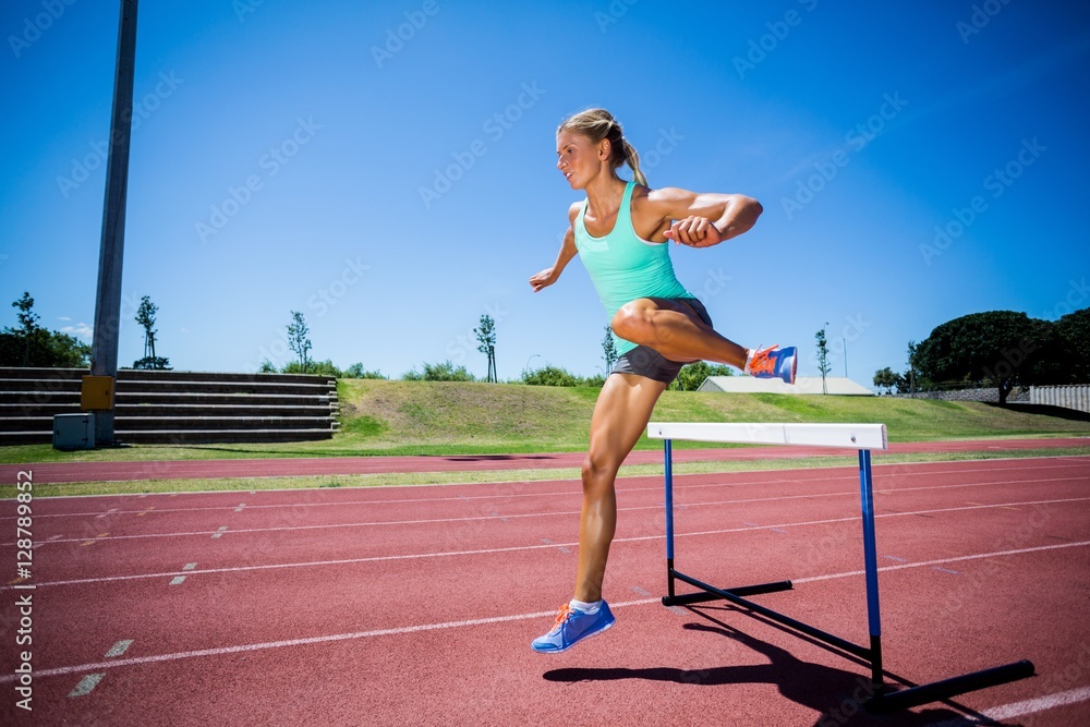 Obraz premium Female athlete jumping above the hurdle