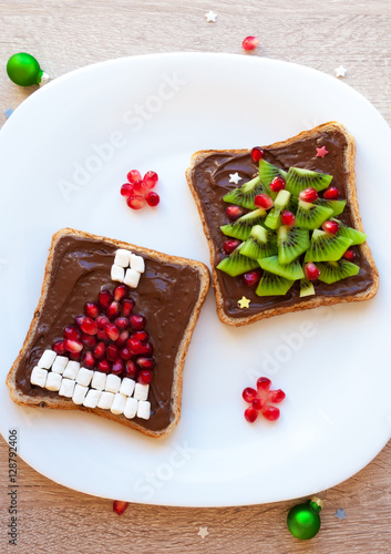 Christmas healthy breakfast or dessert idea for children - toast with chocolate cream, pomegranate Santa hat and kiwi Christmas tree, top view
