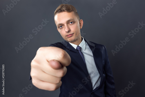 Handsome businessman standing on gray background and and showing fig gesture