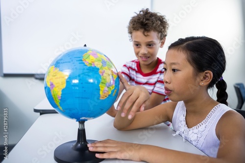 Принти на полотні Elementary boy and girl looking at glob in classroom