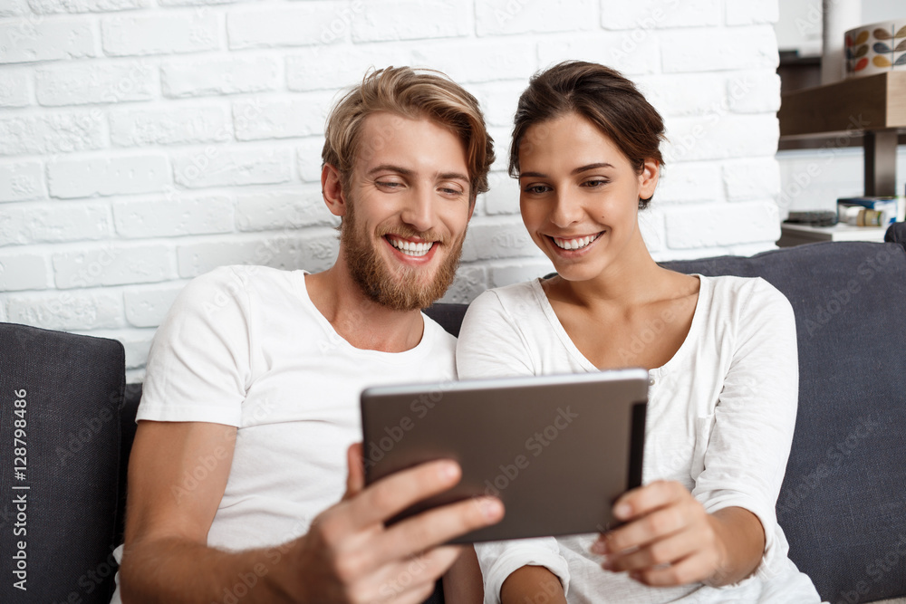 Beautiful couple looking at tablet smiling sitting on sofa home. Beautiful couple looking at tablet smiling sitting on sofa home.