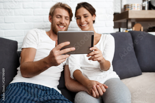 Beautiful couple looking at tablet smiling sitting on sofa home.