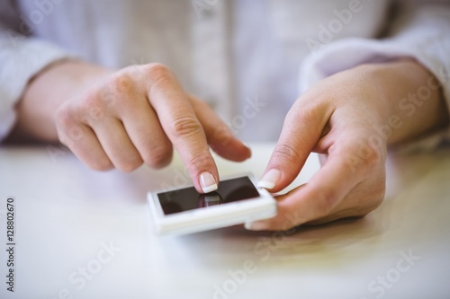 Close-up of businesswoman touching cellphone on desk at office