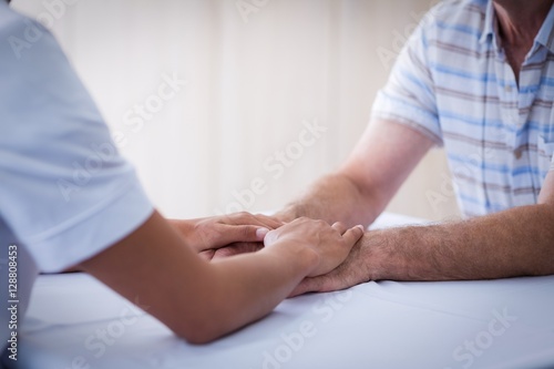 Mid section of female doctor consoling senior man in living room