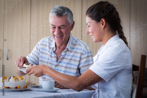 Senior man giving cake to doctor in living room