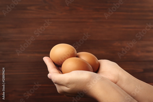 Female hands with eggs on wooden background, closeup
