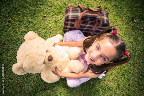 Young girl sitting with a teddy bear and suitcase photo