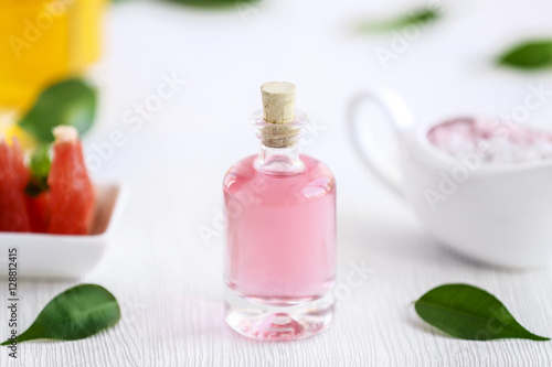 Bottle with essential oil and leaves on wooden table