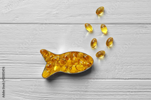 Valokuva Capsules of cod liver oil arranged in a fish shape on white wooden background