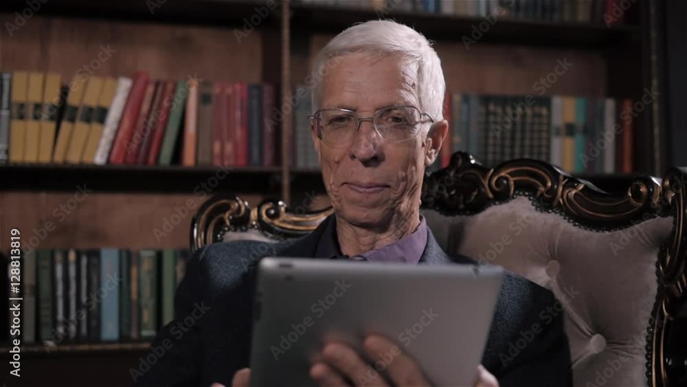 Senior man looking for information on tablet pc in library at home. Happy older man in glasses and modern technology Senior man looking for information on tablet pc in library at home. Happy older man in glasses and modern technology