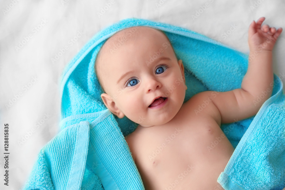 Cute baby with turquoise towel lying on bed sheet Cute baby with turquoise towel lying on bed sheet