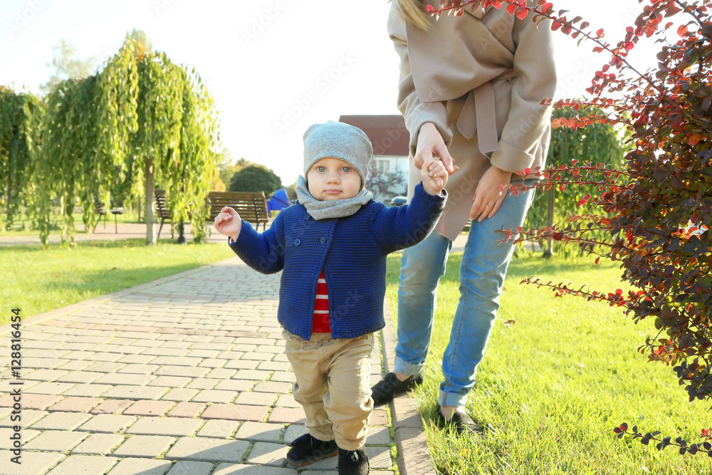 Fototapeta premium Adorable toddler boy learning to walk outdoors with mother's hand in park, childhood development and family support, moment of growth and bonding between parent and child in a natural