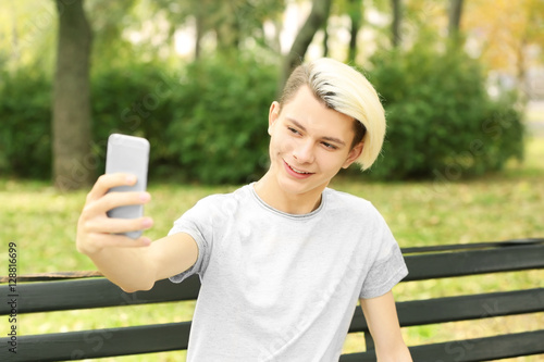 Cute teenager boy sitting with phone in park