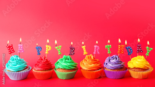 Tasty colorful cupcakes with Happy Birthday candles on red background