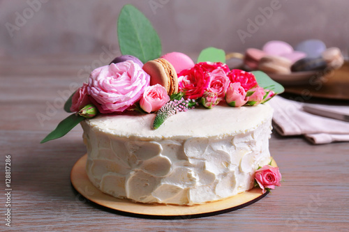 Delicious creamy cake with flowers and macaroons on table