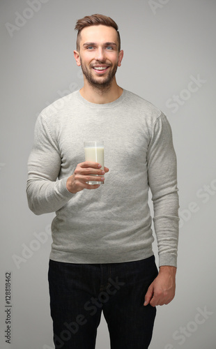 Young man with glass of fresh milk on gray background