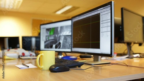 Woman's hand puts yellow mug on office desk during lunch brake. Female engineer screens
