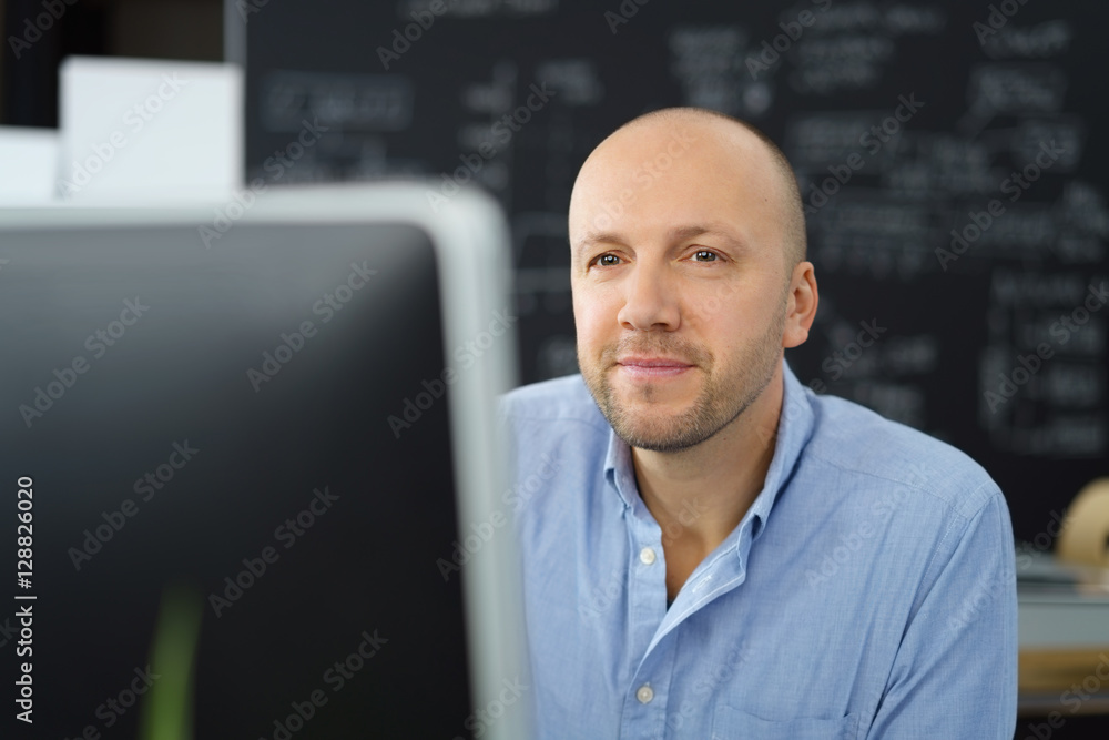 lächelnder geschäftsmann am arbeitsplatz schaut auf seinen pc lächelnder geschäftsmann am arbeitsplatz schaut auf seinen pc