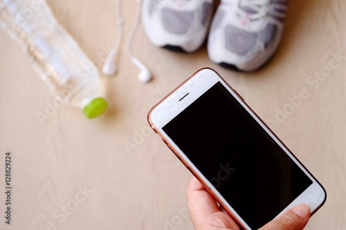 fitness concept with Exercise Equipment on wooden background.White phone with headphones and running shoes on wooden background and copy space.