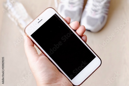 fitness concept with Exercise Equipment on wooden background.White phone with headphones and running shoes on wooden background and copy space.