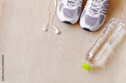 fitness concept with Exercise Equipment on wooden background.White phone with headphones and running shoes on wooden background and copy space.