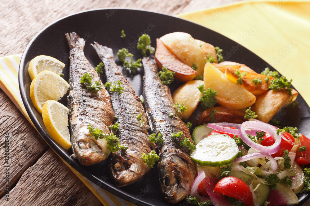 Grilled sardines with roasted potatoes and fresh salad closeup. Horizontal Grilled sardines with roasted potatoes and fresh salad closeup. Horizontal