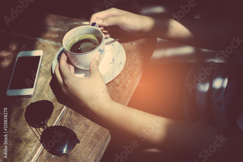 Close-up Of Woman Holding Mobile Phone In Front Of Coffee Cup