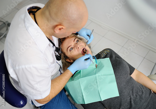 Male dentist examines the mouth and teeth of a patient woman.