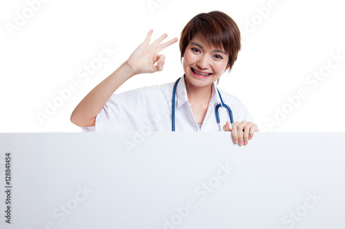 Young Asian female doctor show OK sign  behind blank white billb