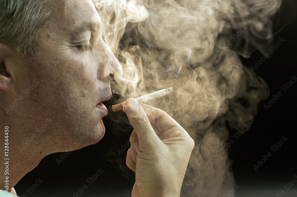 Fototapeta premium Man smoking against a black background, Cigarette addiction. 