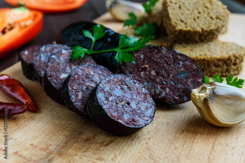 Morcillo (Spanish black pudding, blood sausage), cutting slices, black rye bread in a heart shape, pepper, garlic on a wooden board. Close up. A festive meal on Christmas, Easter