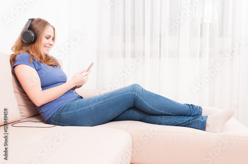 Lady sitting on couch listening to headphones holding smartphone © Catalin Pop