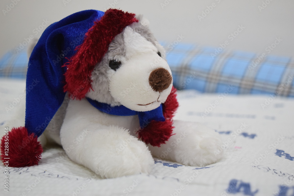Cute santa siberian husky wearing santa hat doll/toy on bed.