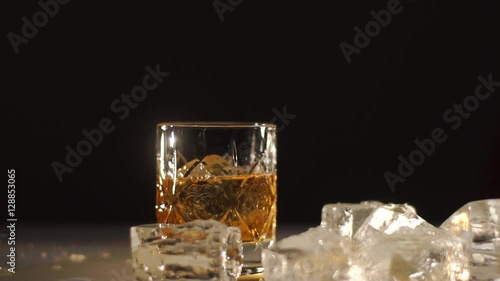 an ice ball falling down into glass with wiskey. Drink is spleshing on the sides. Dark and shadows photo