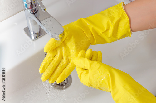Woman hand in yellow rubber glove in water stream