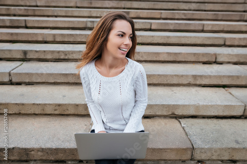 Happy woman smilign and using laptop on ladder photo