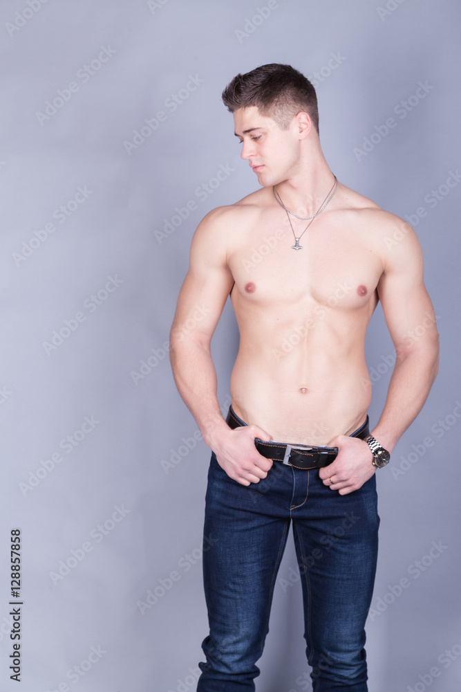 young man with relief muscles in jeans with a naked torso on a gray background