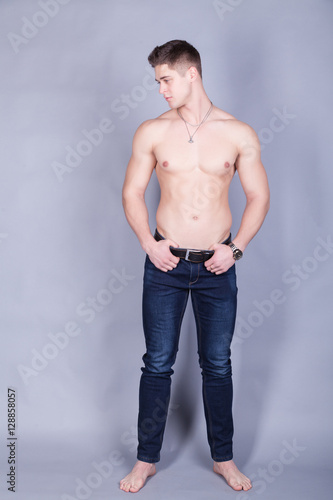 young man with relief muscles in jeans with a naked torso on a gray background