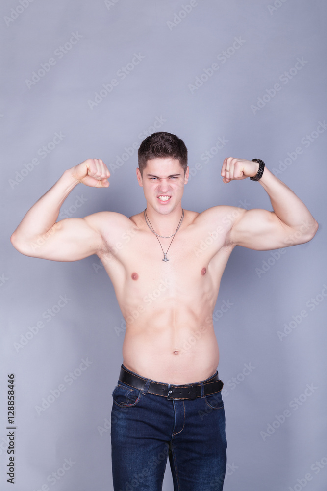 young man with relief muscles in jeans with a naked torso on a gray background young man with relief muscles in jeans with a naked torso on a gray background