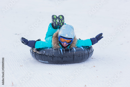 Bild auf Leinwand cheerful girl in a helmet and glasses riding on a sled with high mountains