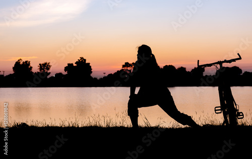 Silhouette woman exercise near bicycle on sunset.