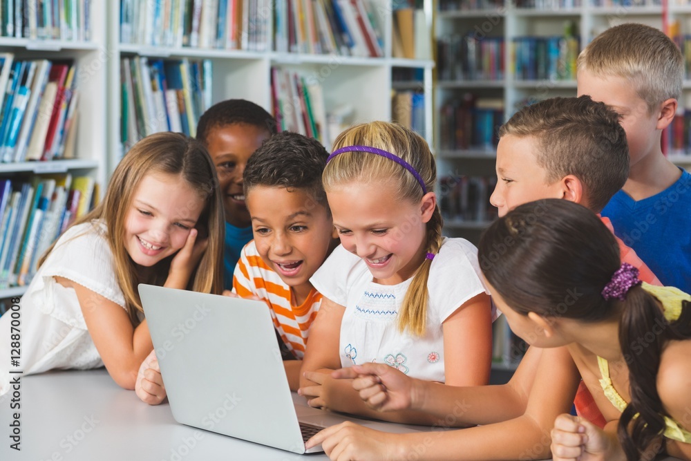 Smiling school kids looking at laptop in library Smiling school kids looking at laptop in library