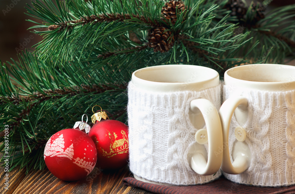 Christmas Decoration with fir twigs, red balls and cups of hot chocolate dressed in knitted warm winter mug holder on wooden background Christmas Decoration with fir twigs, red balls and cups of hot chocolate dressed in knitted warm winter mug holder on wooden background