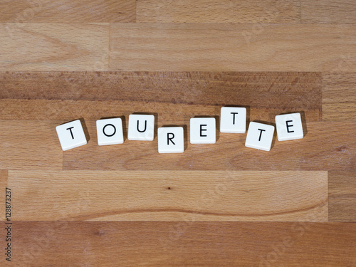 Tourette text on a wooden surface. Tourette Syndrome is one type of Tic Disorder. Tics are involuntary, repetitive movements and vocalizations.  photo