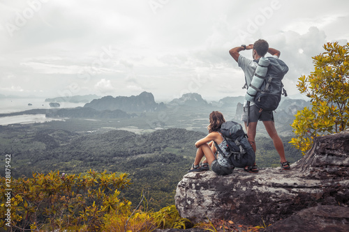 Couple of tourist with backpacks relaxing on top of a mountain and enjoying the view of valley